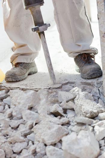 Using a jackhammer to locate a broken drain pipe under a cement floor.